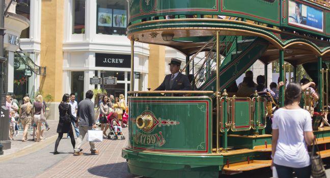 A historically styled trolley car tram carries passengers past shoppers and tourists at The Grove shopping center in Los Angeles